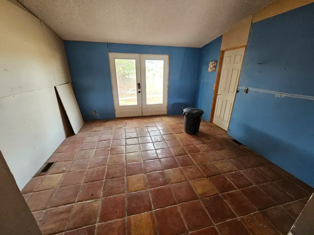Emptied room with a bare tile floor and a single trash can left standing, part way through a full house cleanout.