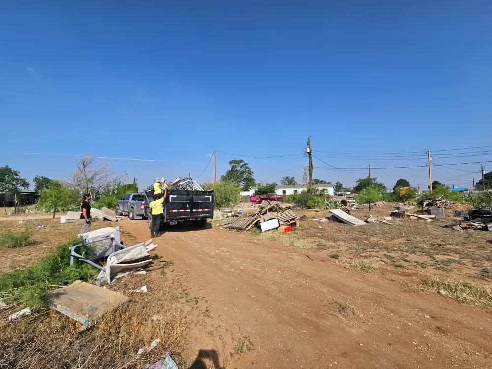 Two crew members loading broken lumber and household debris into the Big Fish dump trailer on a cleared lot outside Big Spring, Texas.