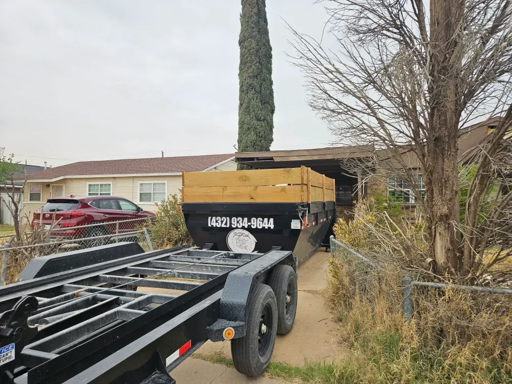 Big Fish Rentals container with timber side extensions squeezed onto a narrow side drive beside a house, the hook-lift trailer waiting on the path in front of it.