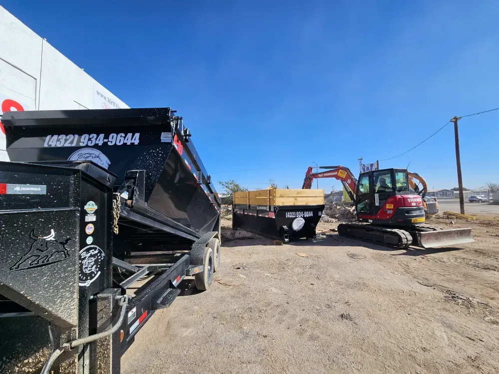 Two Big Fish Rentals containers staged on a cleared commercial lot in Big Spring, Texas, while a contractor's compact excavator works a demolition pile behind them.