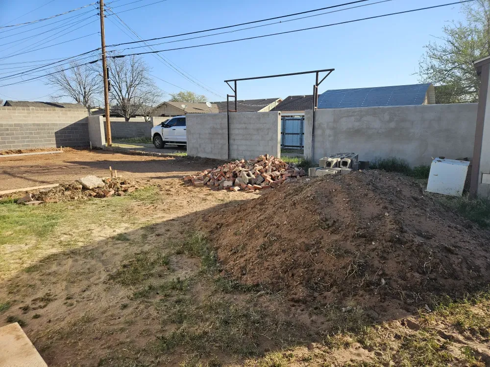 Broken brick, cinder block and a long mound of excavated dirt heaped in a walled back yard in Odessa, Texas, with the Big Fish Rentals pickup waiting at the gate.