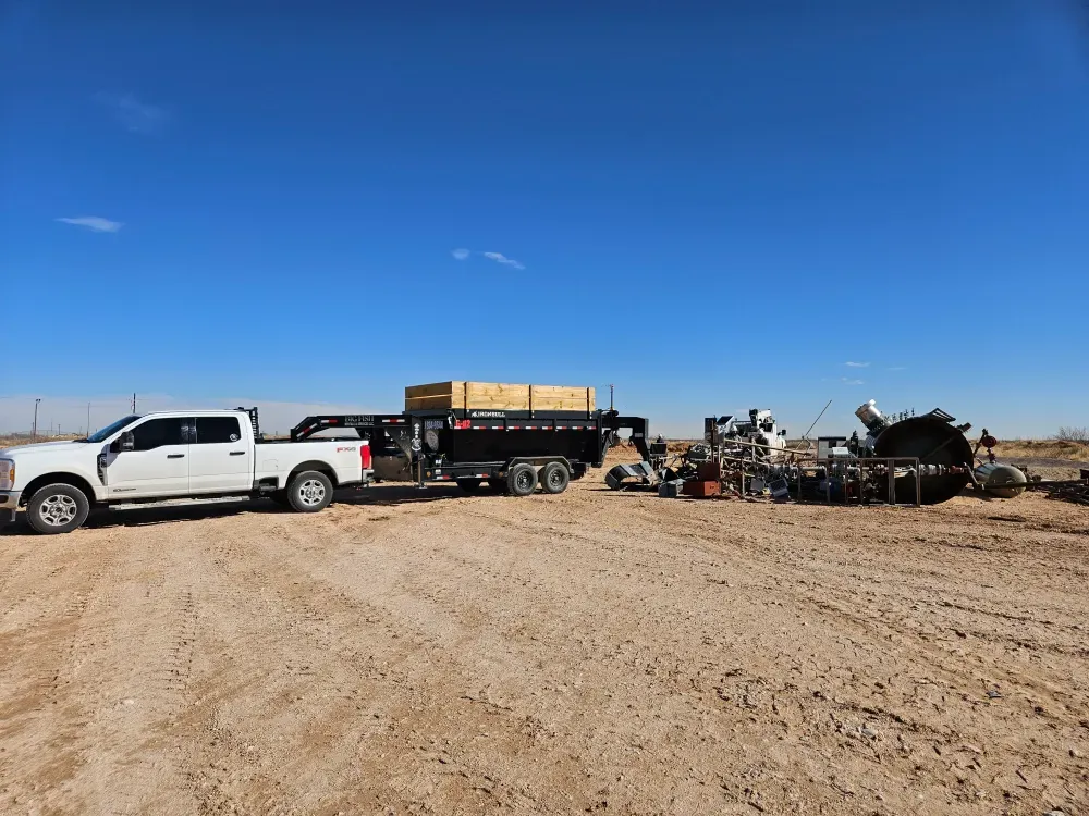 Big Fish Rentals pickup and gooseneck dump trailer parked on open desert caliche near Crane, Texas, beside a heap of scrap steel, with a wide West Texas sky above.