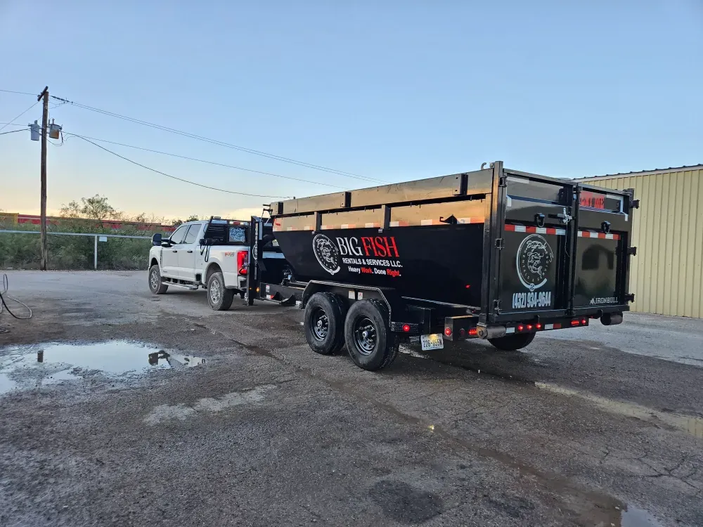 The Big Fish Rentals pickup at dusk with the branded dump trailer hitched behind it, the company name, tagline and phone number lettered across the side.