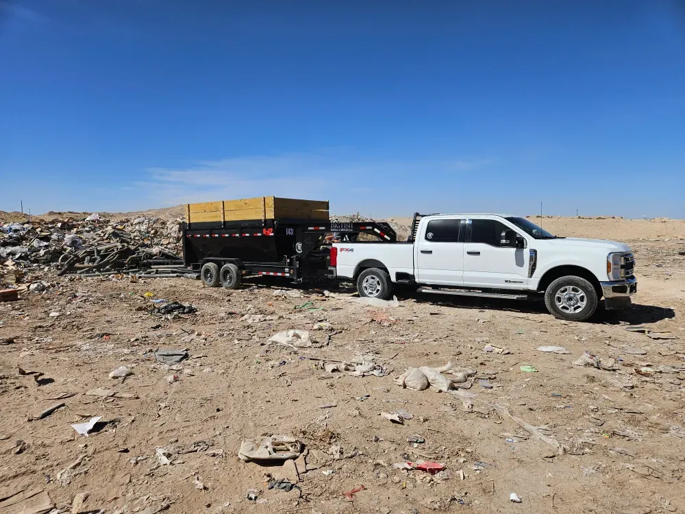 The Big Fish Rentals truck and dump trailer parked on the working face of a landfill, bare caliche and low earth berms under a deep blue sky.