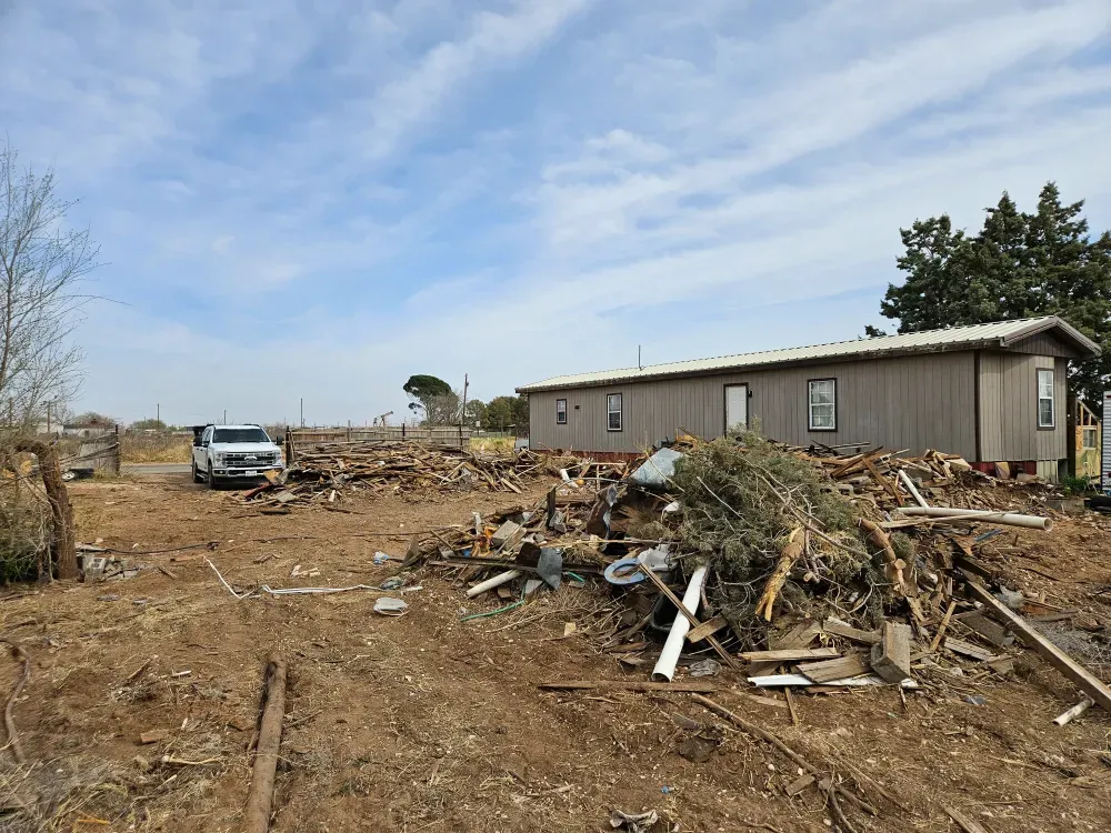 Contents and torn-out material from a whole-property cleanout spread across the yard beside a single-storey house in West Odessa, Texas, with the truck backed in at the gate.