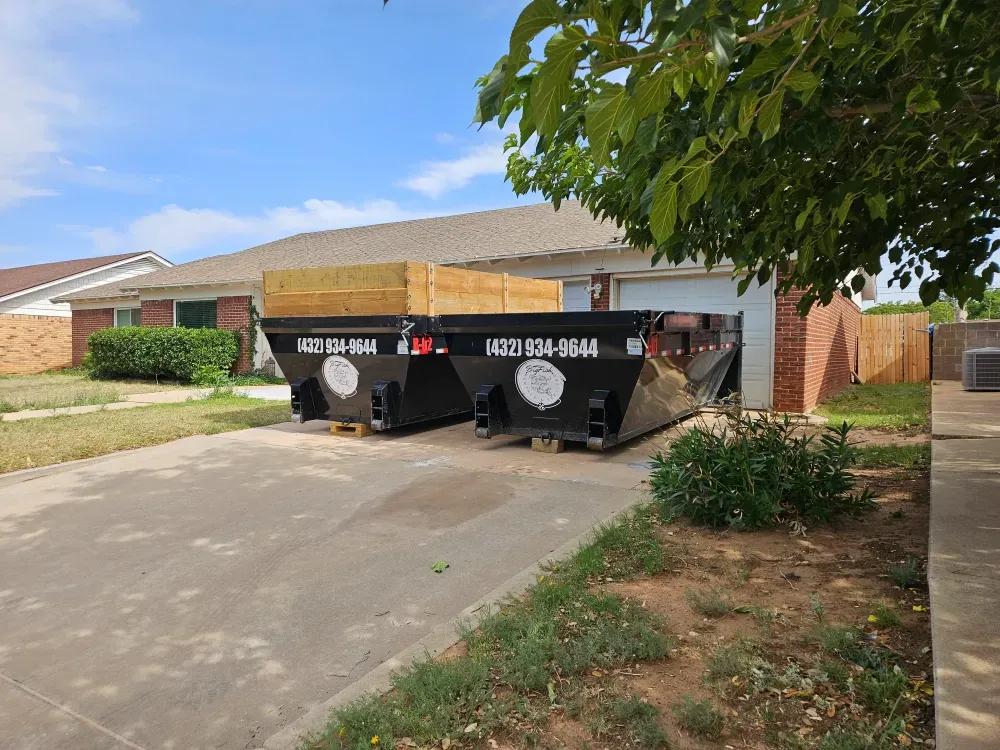 Two Big Fish Rentals roll-off containers with timber side extensions parked side by side on a brick house driveway in West Odessa, Texas.