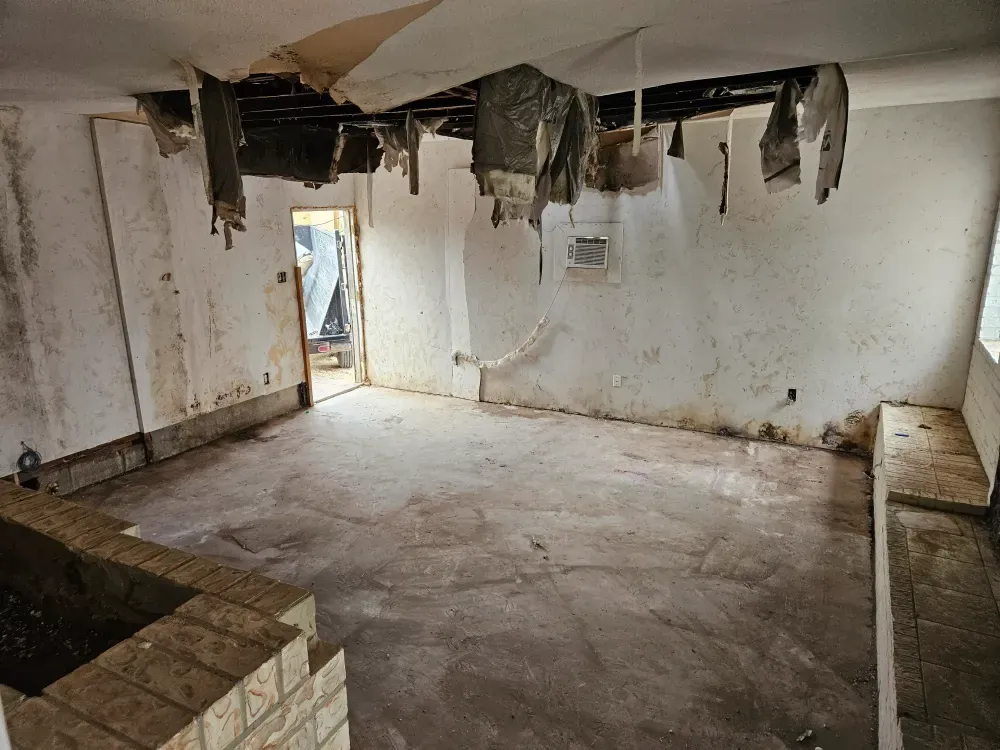 Water-damaged room stripped back during a cleanout in West Odessa, Texas: ceiling tiles down, insulation hanging, stained walls and a bare concrete floor, with a Big Fish Rentals trailer visible through the open door.